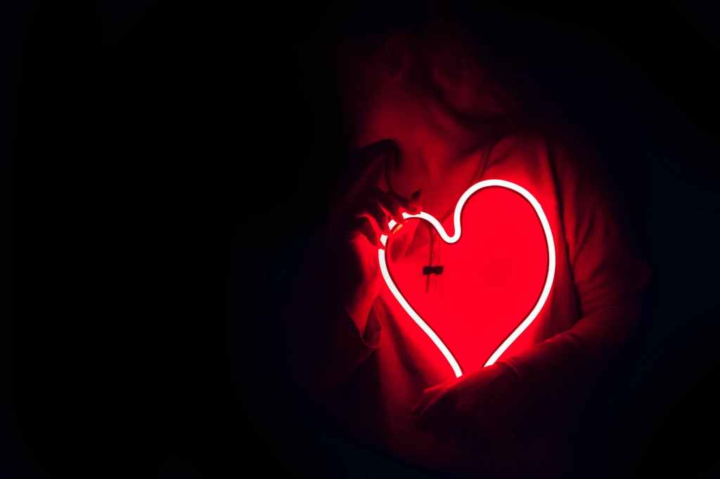 A dark background a person holding a red neon heart.