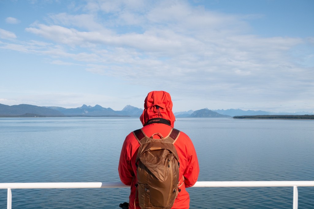 A person facing away from the camera. They are wearing an orange rain coat and a brown backpack.