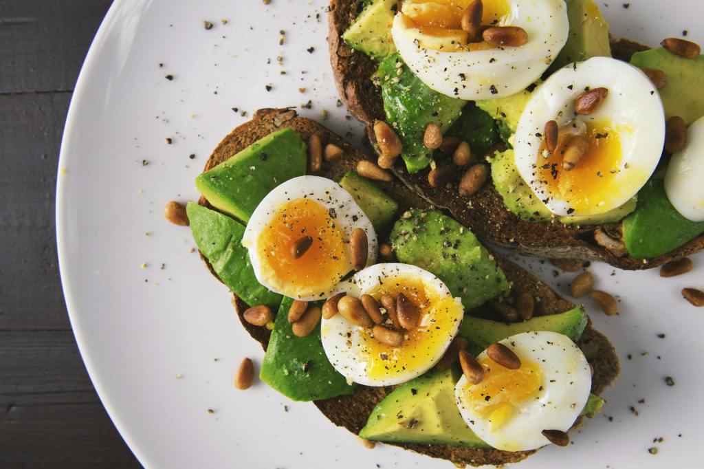 Gourmet boiled eggs and avocado on toast. Toasted pine nuts and cracked pepper are sprinkled on top.